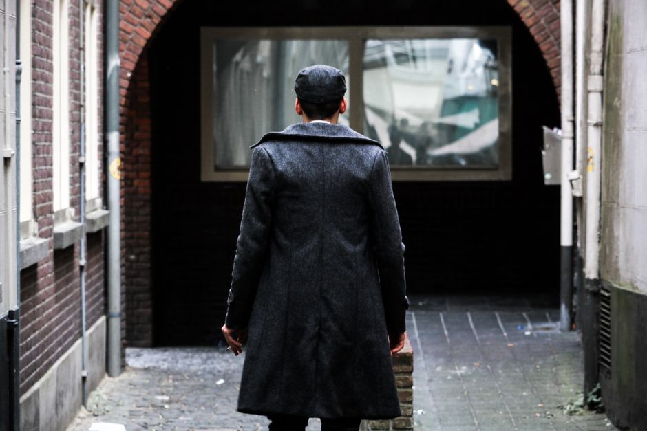 A man in a coat walks through a brick-walled urban alley during the day, capturing a moody city vibe.