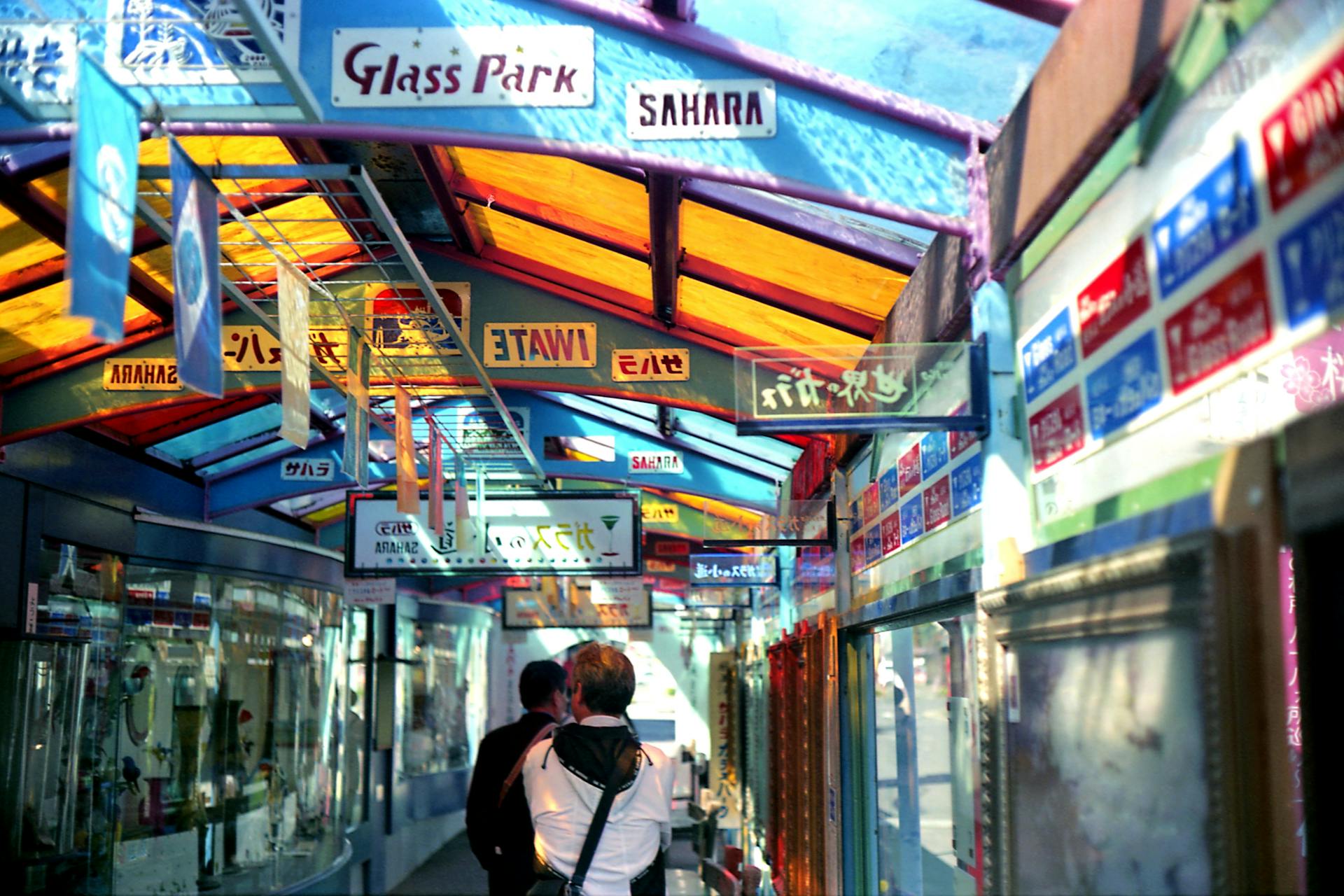 A lively, colorful walkway in a covered market with diverse international signage.