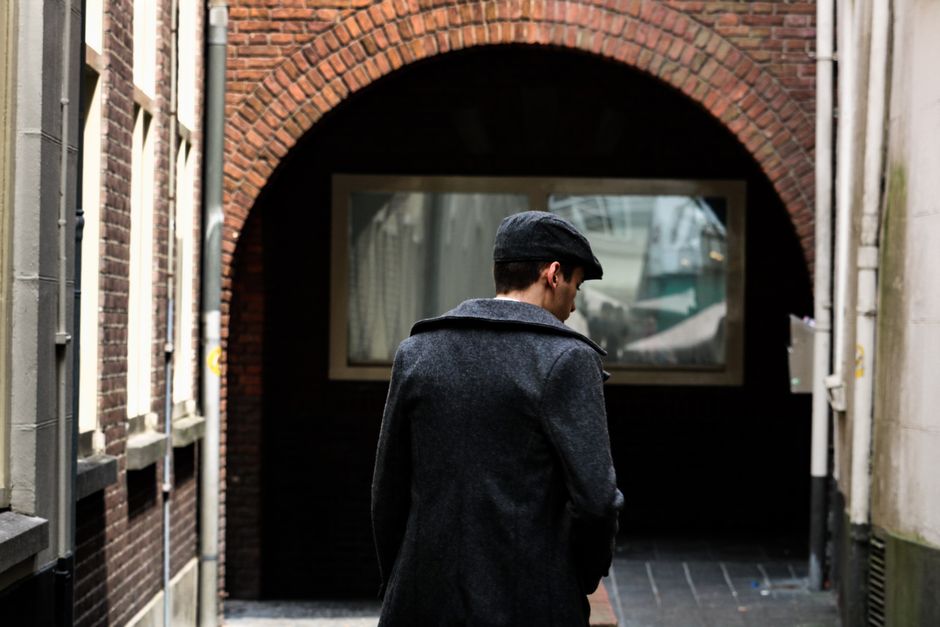 A man in a coat and cap walks through a brick archway in an urban alleyway.