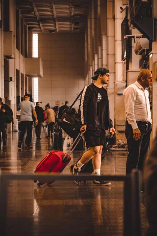 Free A young traveler with a red suitcase navigating a busy terminal. Stock Photo