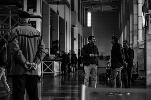 Grayscale Photo of Men Talking Inside a Building