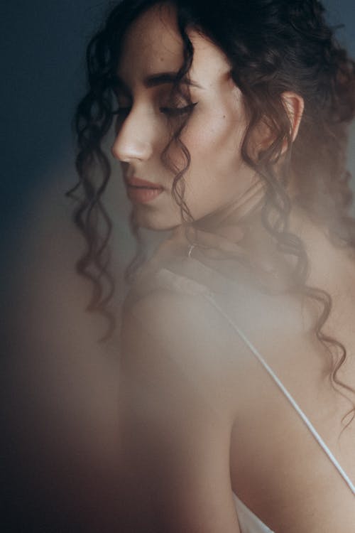 Woman in Curly Hair Wearing White Spaghetti Top while Posing at the Camera