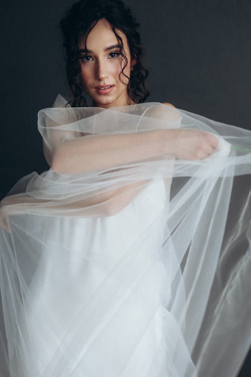 Woman in White Dress Covered with Veil while Posing at the Camera