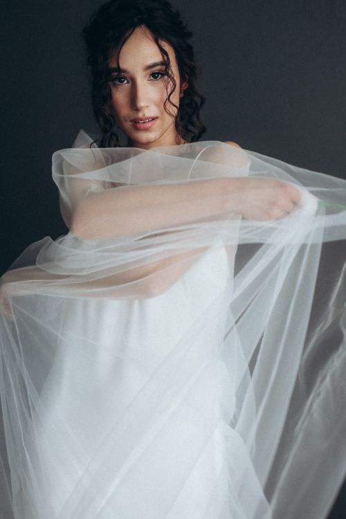 Free Portrait of a woman in a white dress with a flowing veil against a dark background. Stock Photo