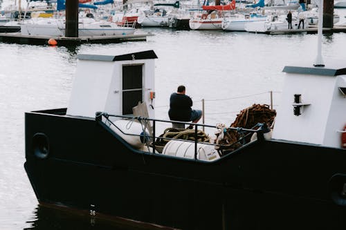 Man in Black Shirt Sitting on Black and White Boat