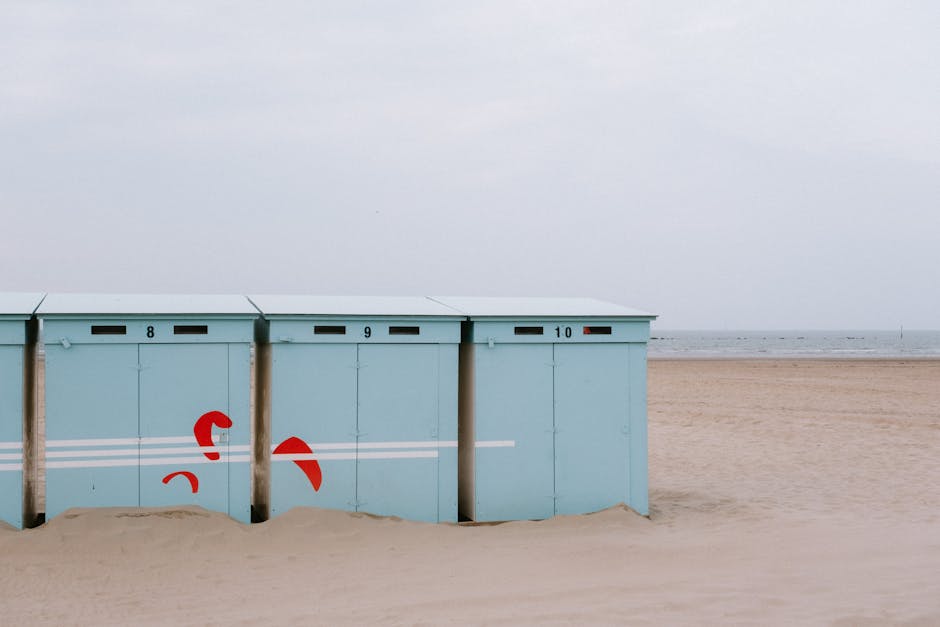 Minimalist beach huts on a quiet sandy beach with a calm sea in the background.