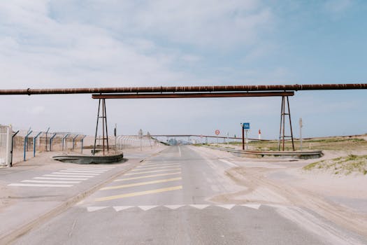 A coastal road featuring industrial pipelines, fences, and clear skies, ideal for industrial themes.