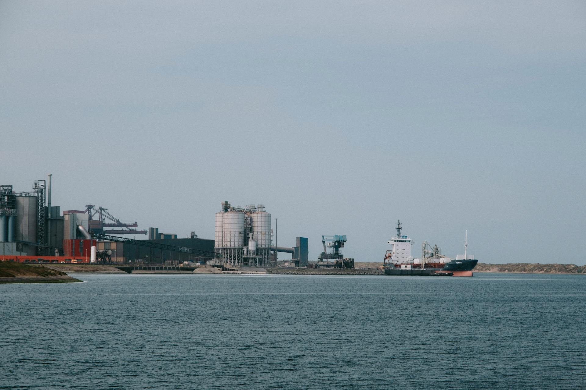 Cargo ship docked at an industrial port with silos and machinery, showcasing maritime and manufacturing industries.