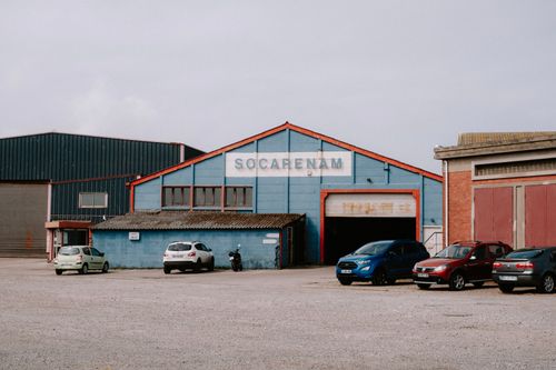 Free Exterior view of an industrial warehouse with various cars parked in front. Stock Photo