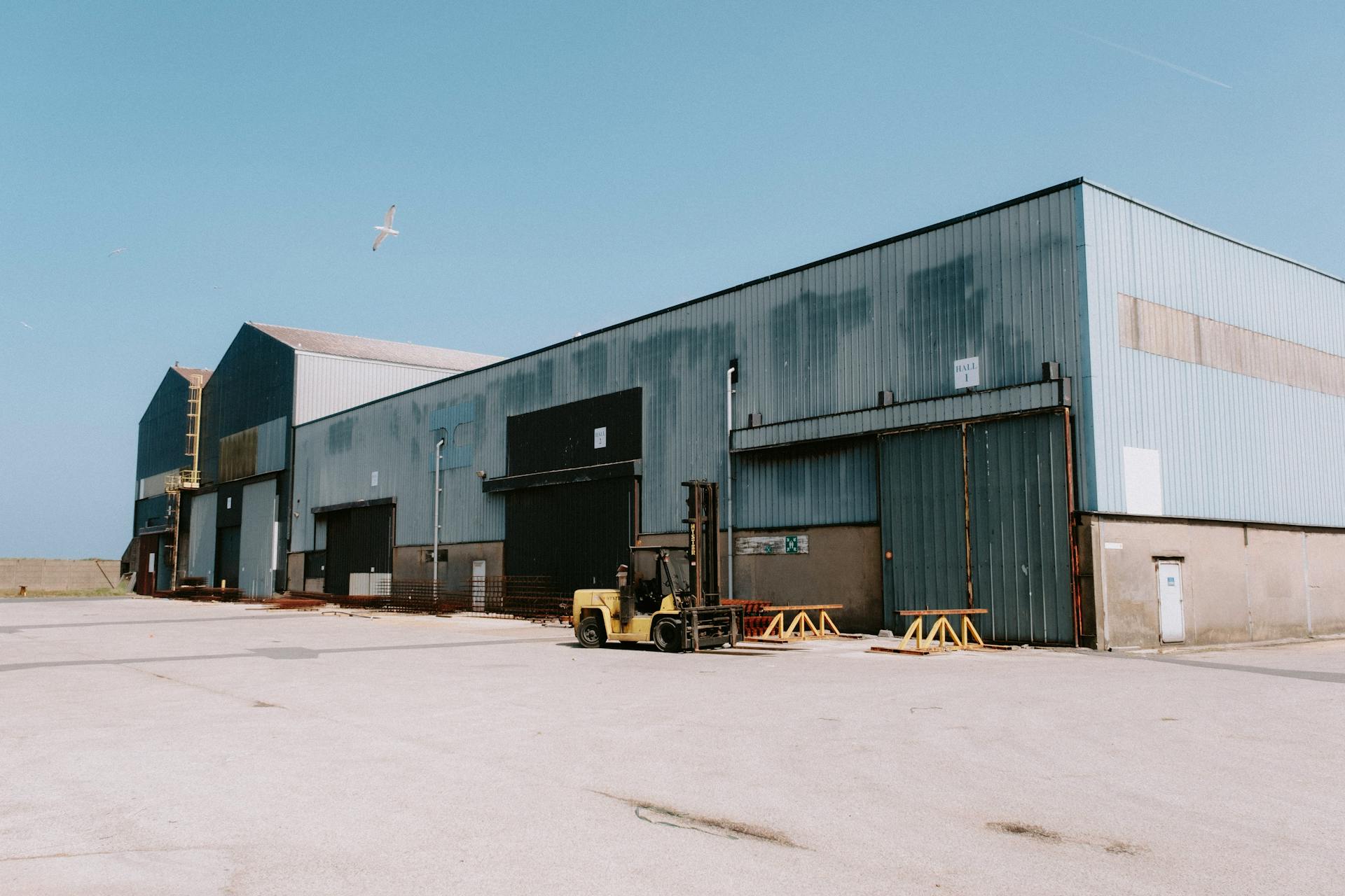 A large industrial warehouse with a forklift and a bird flying overhead.