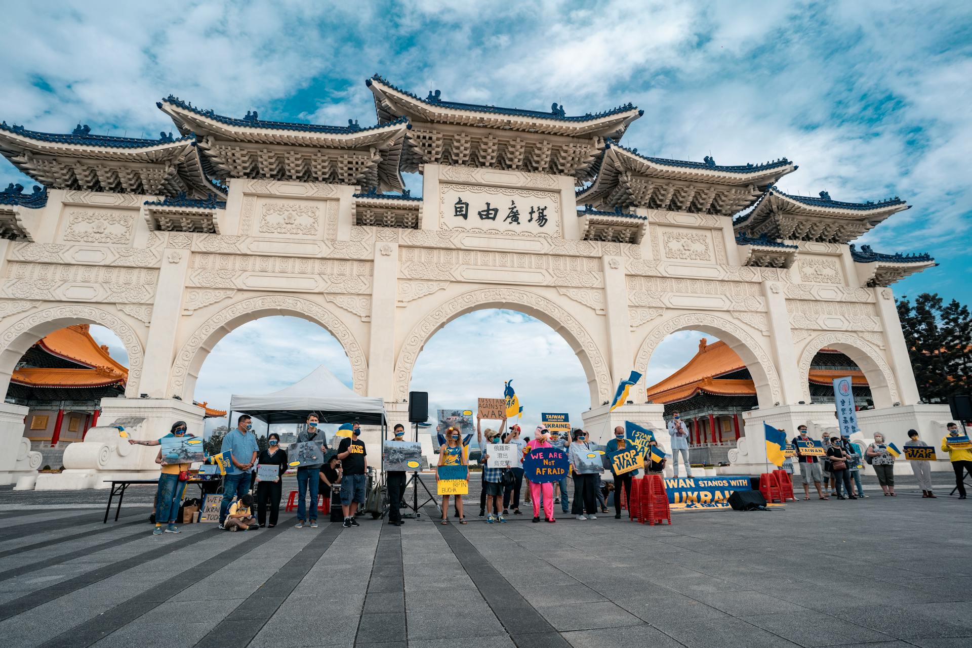 People gather at an iconic gateway holding flags and banners for a protest.