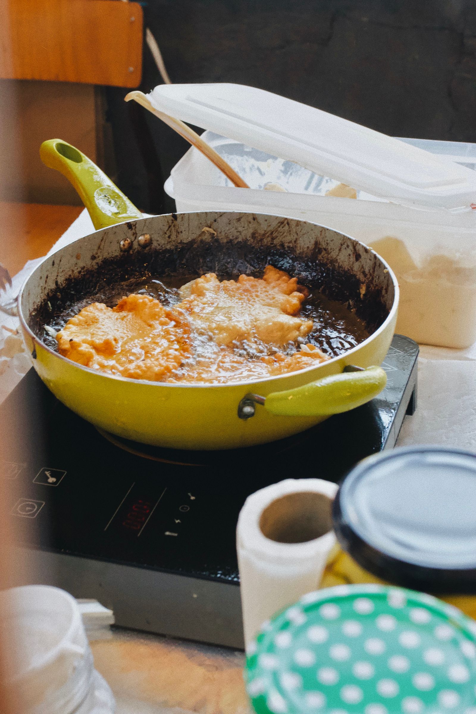 Close-up of frying chicken in a green pan using an induction stove in a home kitchen.