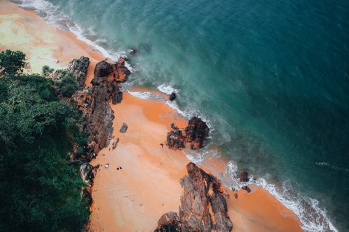 Free A breathtaking aerial shot of a rocky coastline with vibrant blue water and lush greenery, perfect for nature and travel themes. Stock Photo