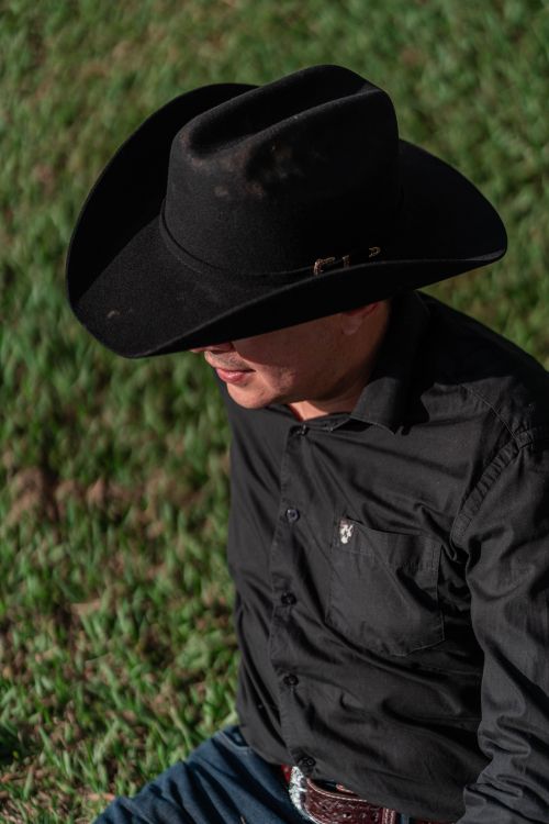 Free A man in a black cowboy hat sits outdoors on green grass during the day. Stock Photo