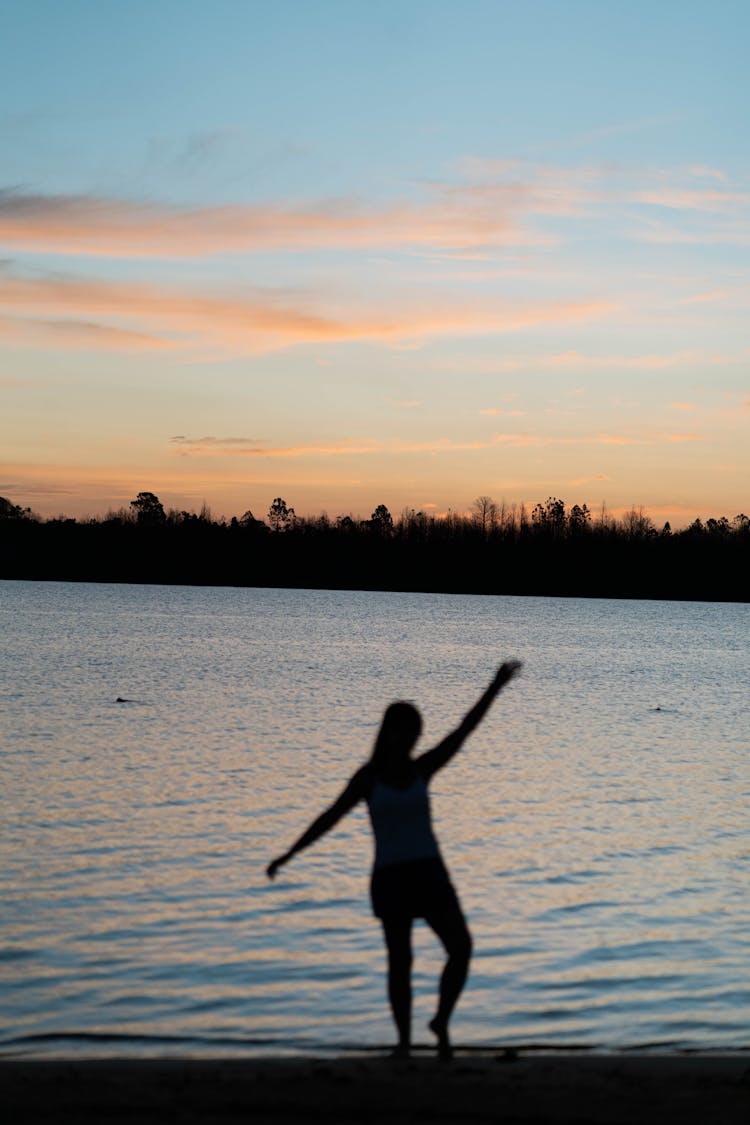 Silhouette Of Woman Dancing On Beach On Sunset