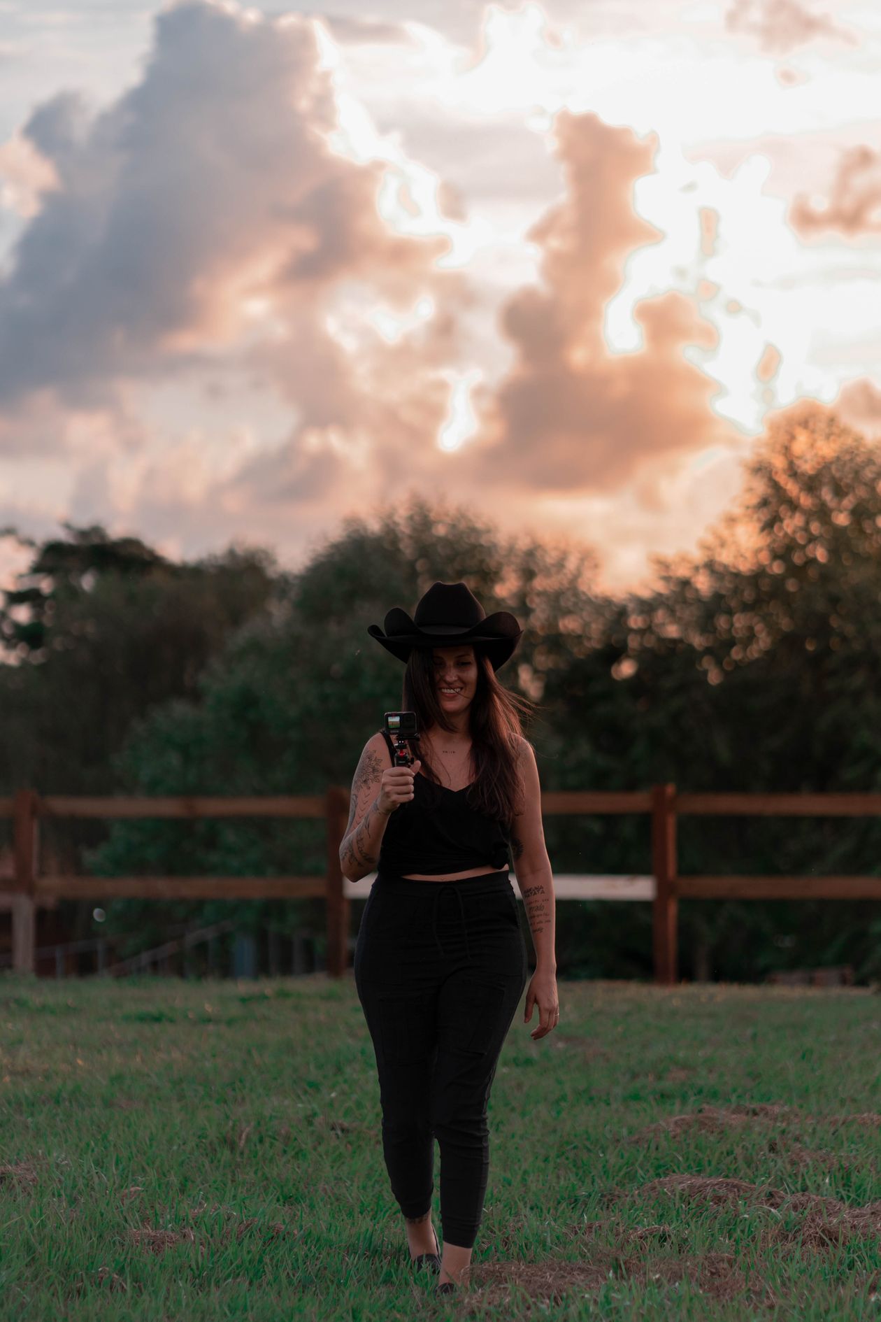 Woman in a black cowboy hat walking across a grassy field at sunset