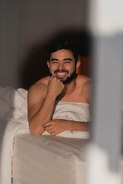 Free A bearded man smiling while laying in bed, capturing a relaxed morning vibe. Stock Photo