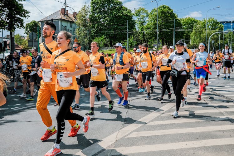 Group Of People In Orange Shirts Running On Asphalt Road