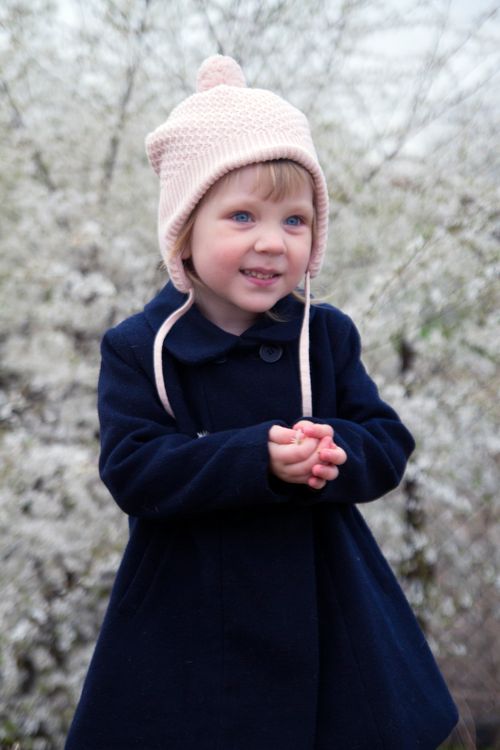 Free Adorable toddler in a navy coat and pink knit hat smiles in a snowy outdoor setting. Stock Photo