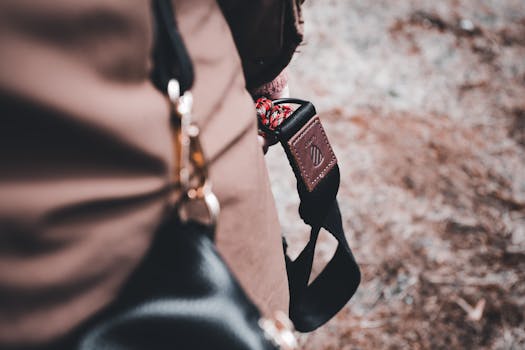 A detailed close-up of a black leather bag with a black strap outdoors on a muted background.