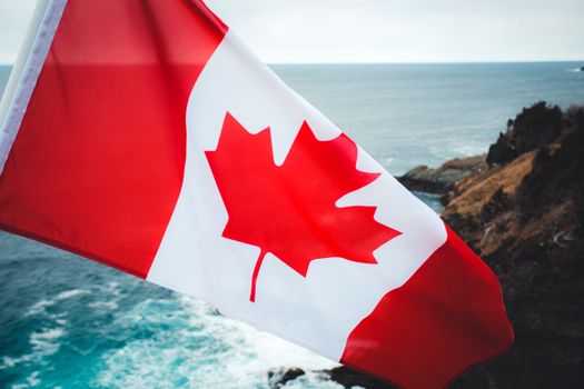 Bright Canadian flag waving over a rocky ocean view, showcasing national pride.