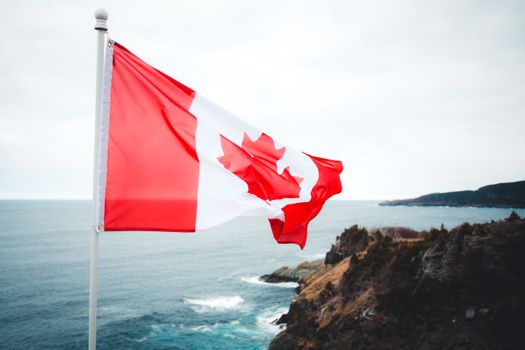 Canadian flag waving over a beautiful, rugged coastline with ocean views.
