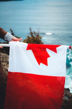 A person holding a Canadian flag on a coastal cliff, showcasing patriotism and nature.