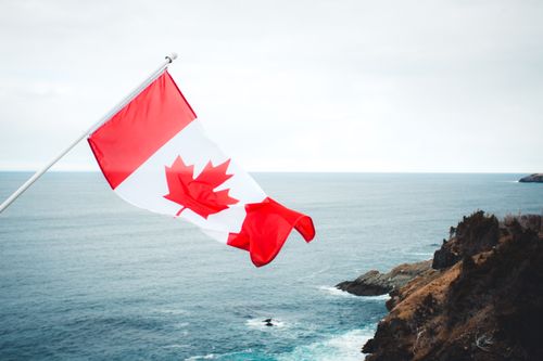 Free Vibrant Canadian flag waves against a serene ocean backdrop, showcasing national pride. Stock Photo