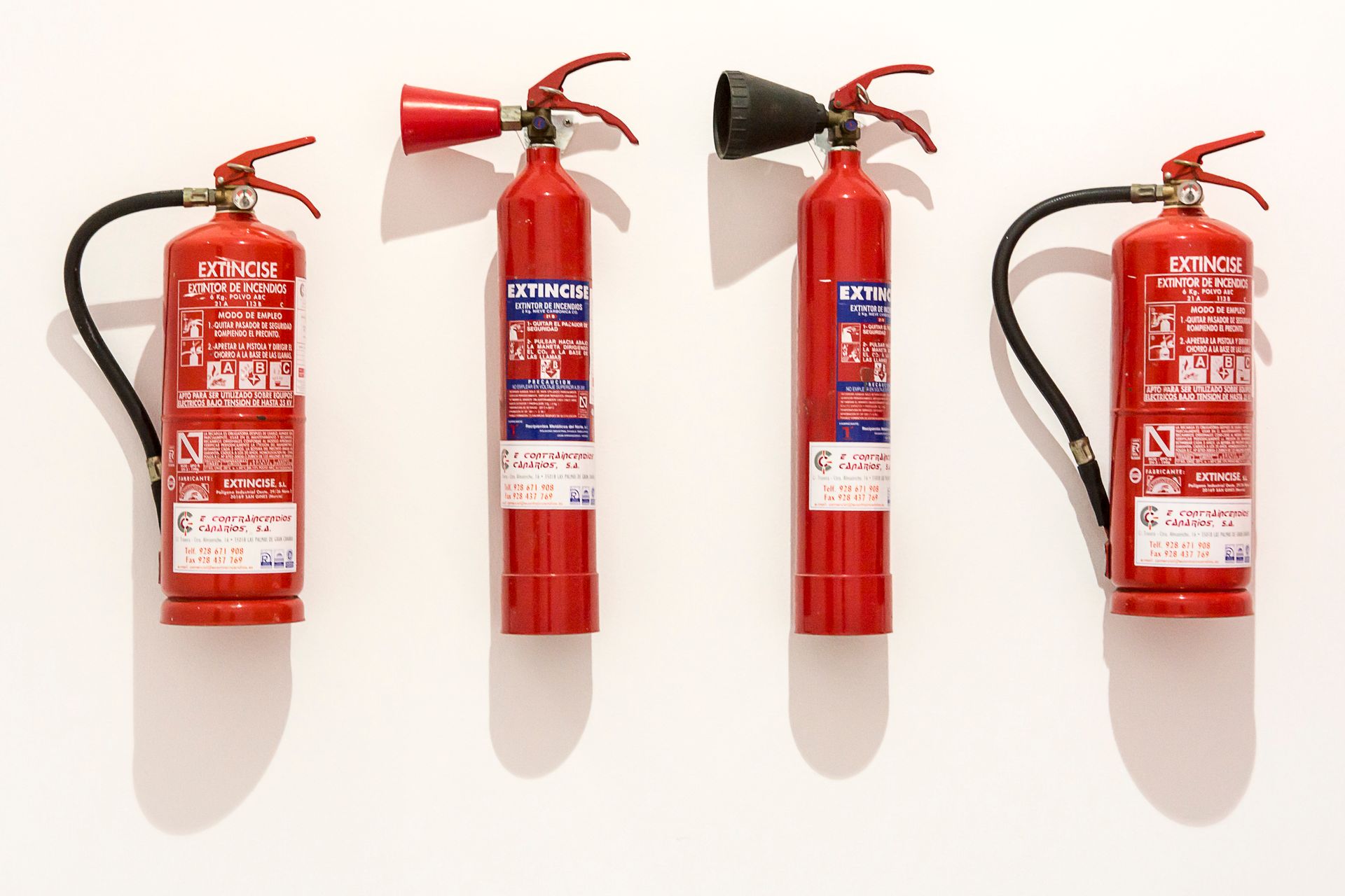 Four red fire extinguishers hanging on a clean white wall in an orderly fashion.