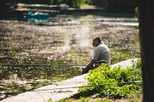 A Man Holding a Fishing Rod while Sitting on the Ground in front of a Lake