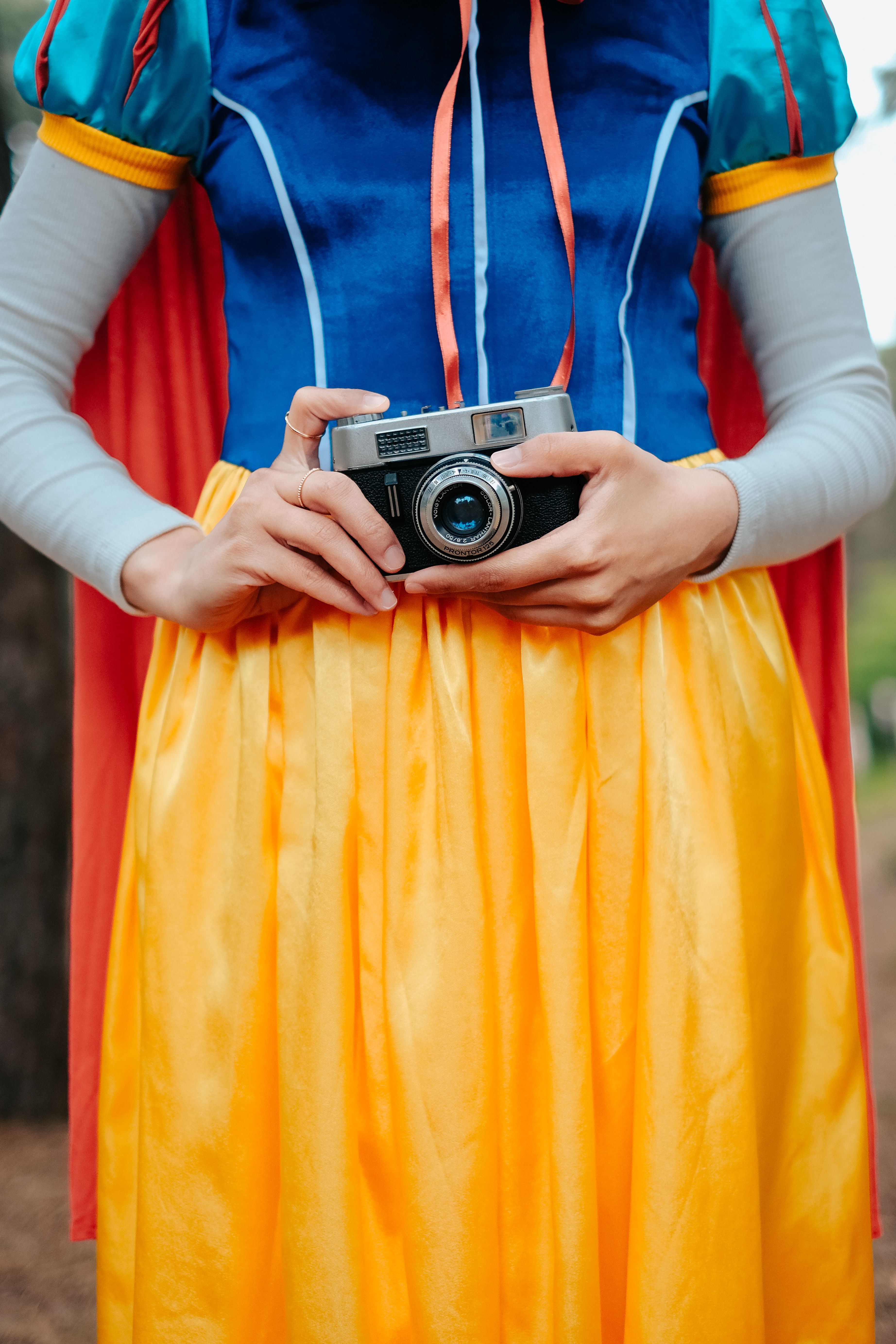 A person in a fairy tale costume holds a vintage camera in an outdoor setting.
