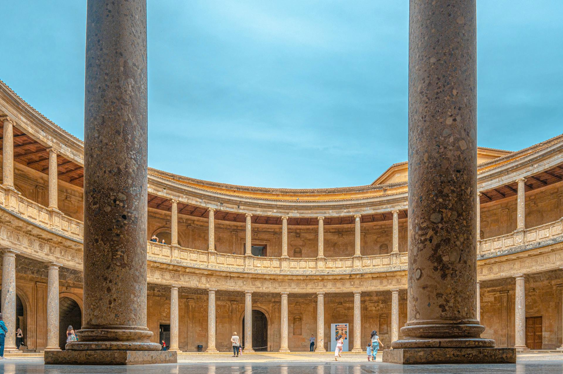 Circular interior of the Palace of Charles V in Granada with grand columns and people exploring.