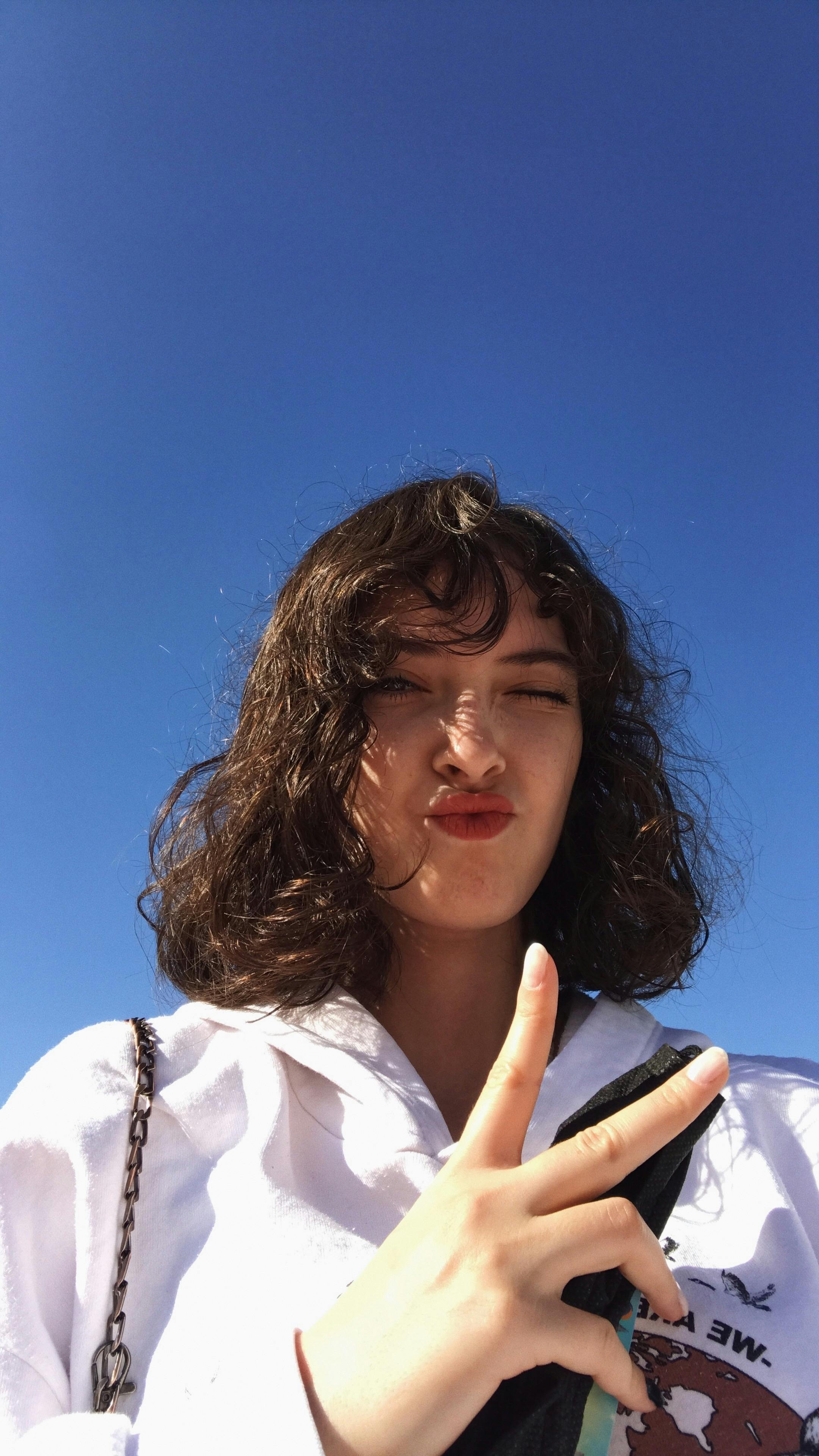 A young woman gives a peace sign under a vivid blue sky, exuding confidence and joy.
