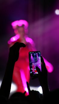 Silhouette capturing a concert with vibrant lights on a smartphone screen.