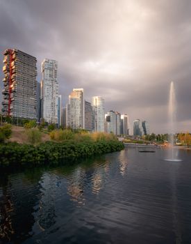 Captivating city skyline with dramatic clouds reflected in a river and water fountain.