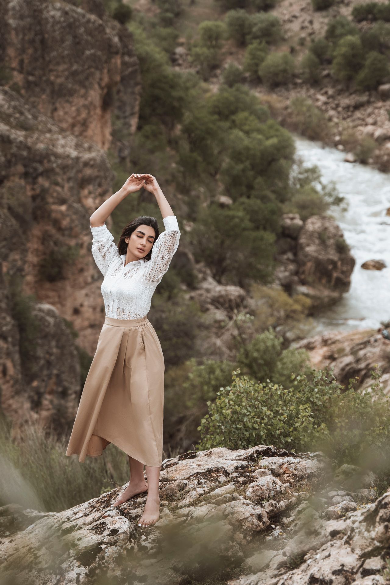 Woman in a white lace top and tan midi skirt standing on rocks