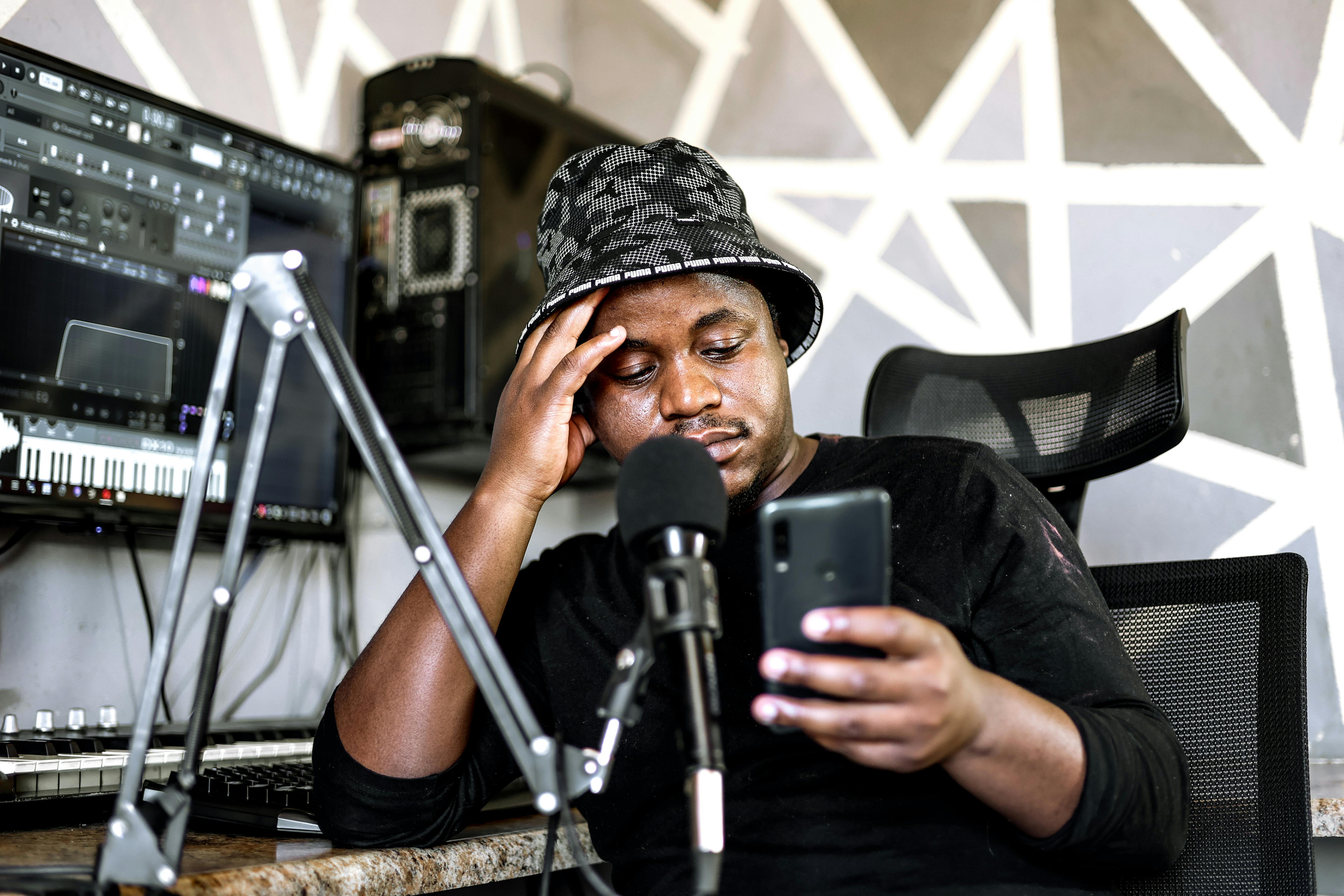 Musician using smartphone and microphone in a modern home recording studio.
