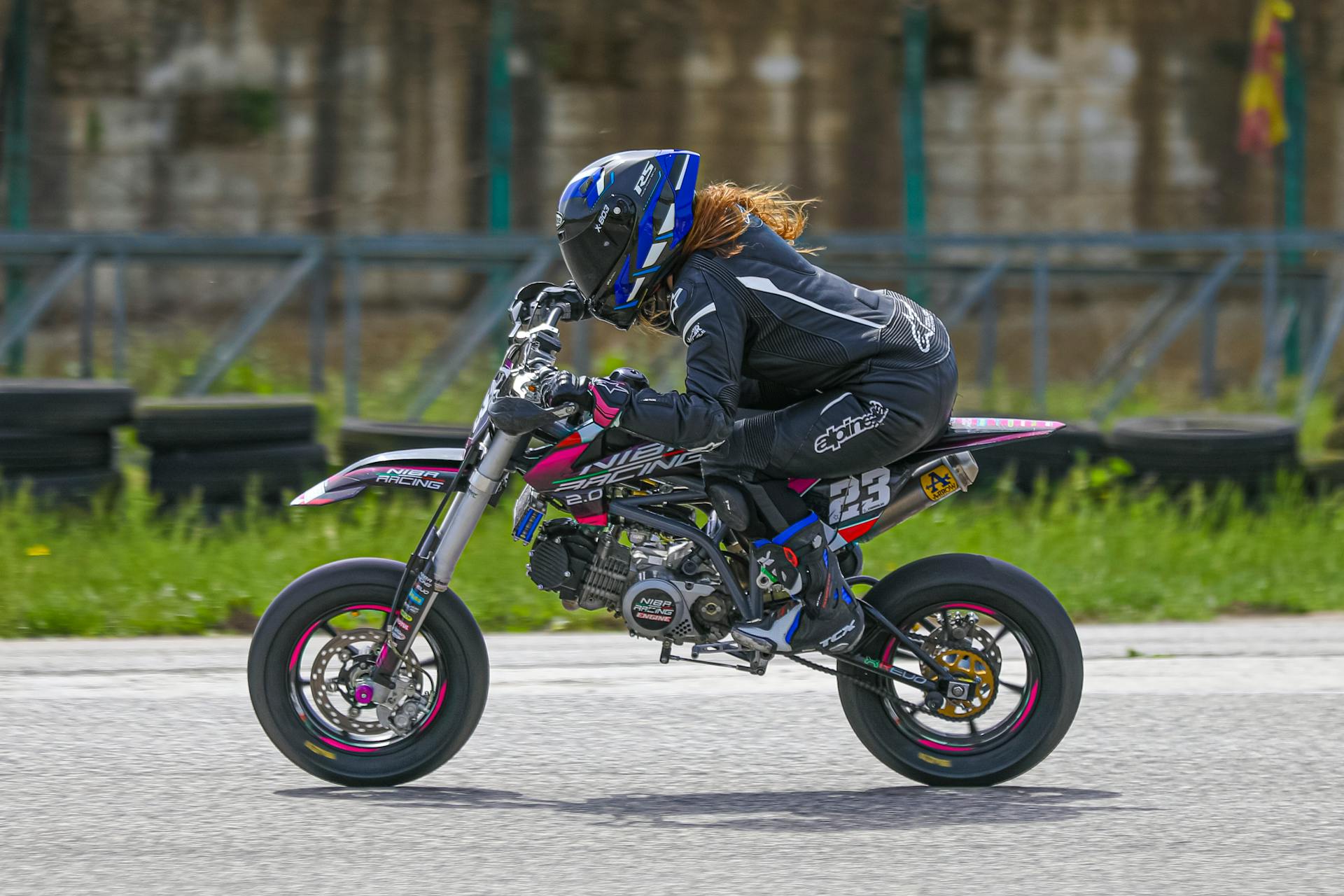 A woman wearing safety gear races on a mini dirt bike outdoors, showcasing speed and control.
