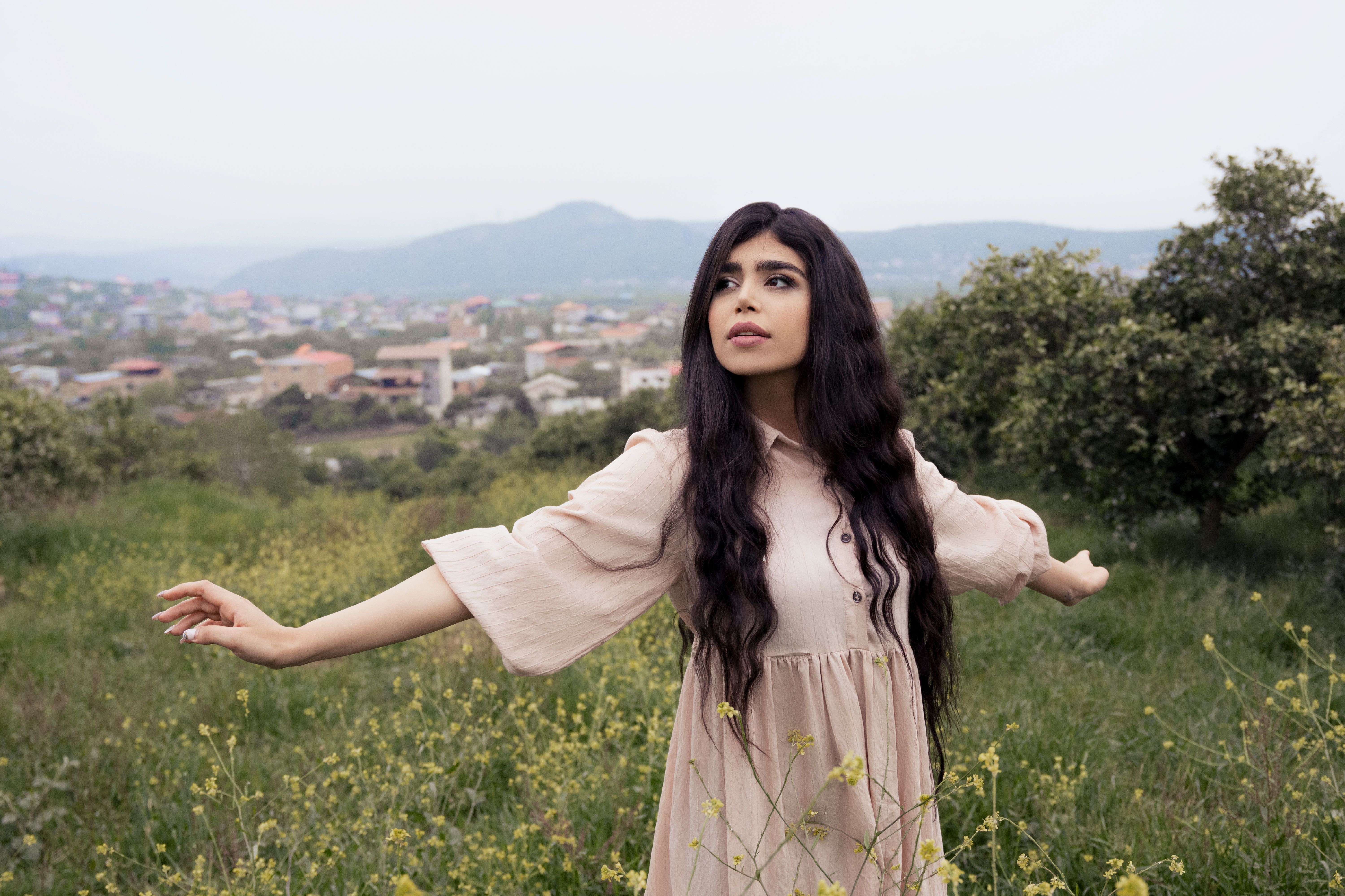 A serene portrait of a woman in a beige dress posing in a lush grass field.