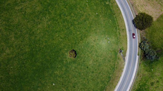 Drone shot of a red car on a winding road through lush green fields in Chocontá, Colombia.
