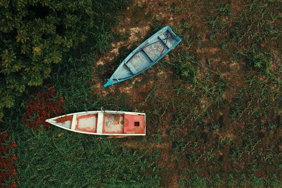 Aerial shot of two weathered boats on grass with lush greenery surrounding them.