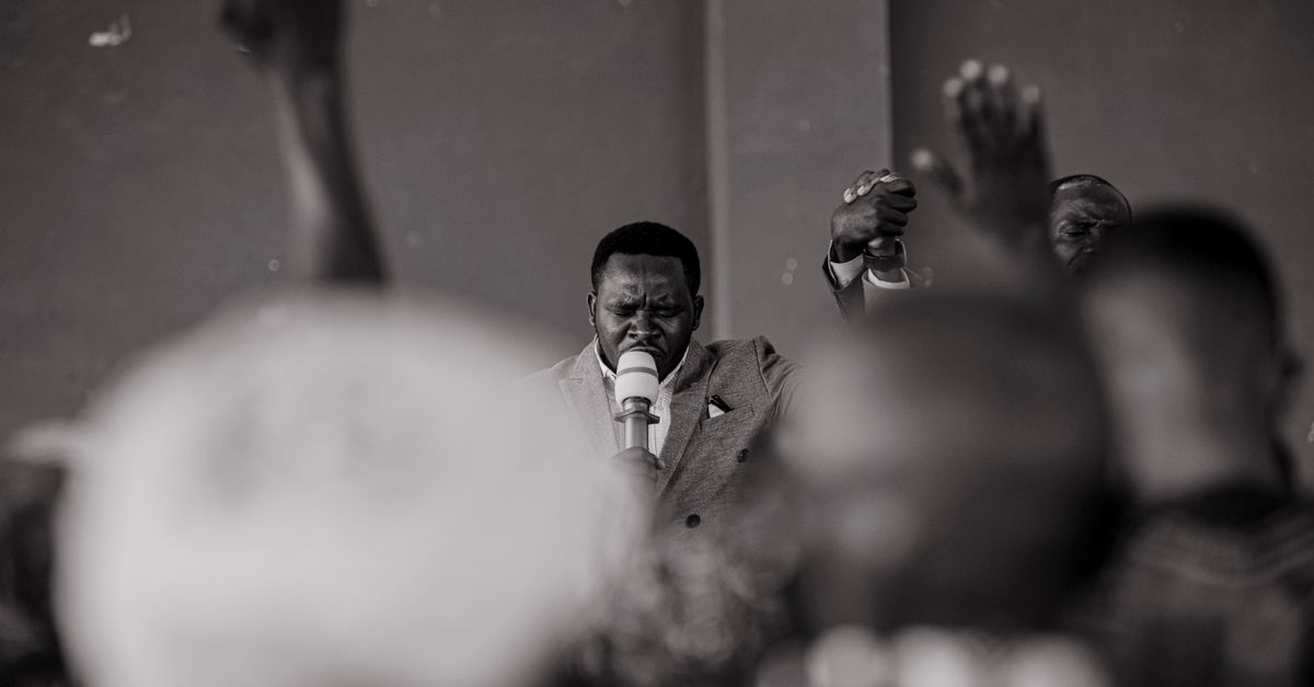 A pastor speaking passionately at a podium, with a congregation raising hands in worship