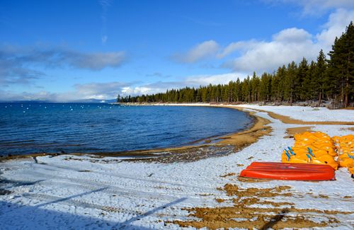 Free Snow-covered Zephyr Cove beach with kayaks and clear lake view under a bright winter sky. Stock Photo
