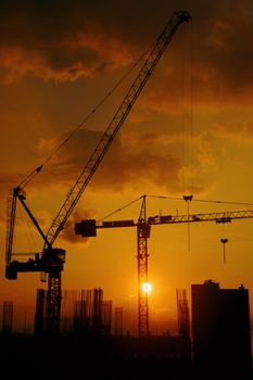 Construction cranes silhouetted against a vibrant sunset sky, creating an industrial skyline.