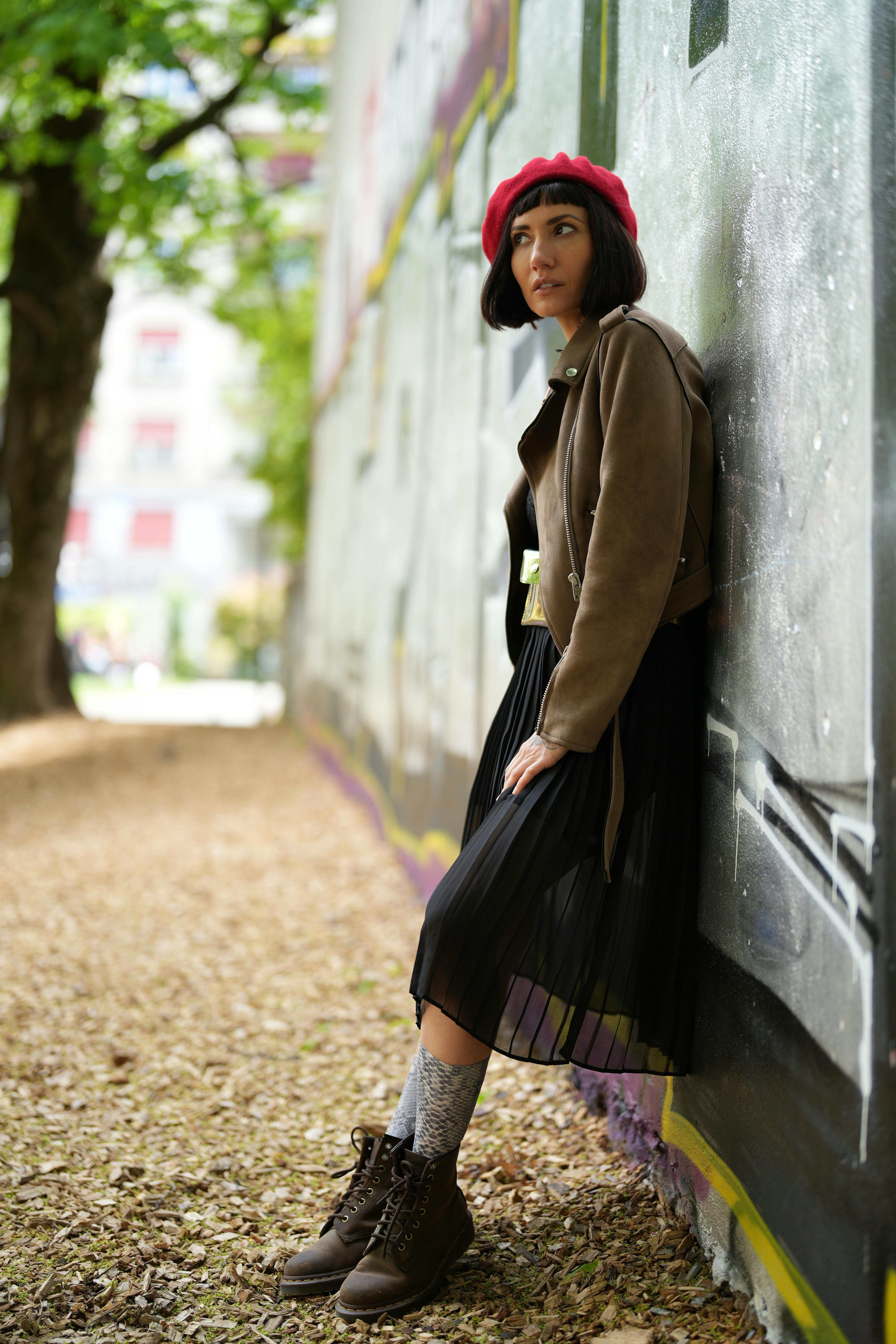 Stylish woman in red beret leaning against graffiti wall in Geneva.