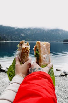 Two people holding sandwiches with a scenic view of an alpine lake in Grainau, Germany.