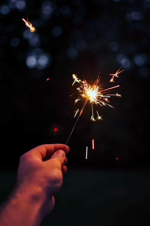 Free A person holding a bright sparkler outdoors in a festive night setting. Stock Photo