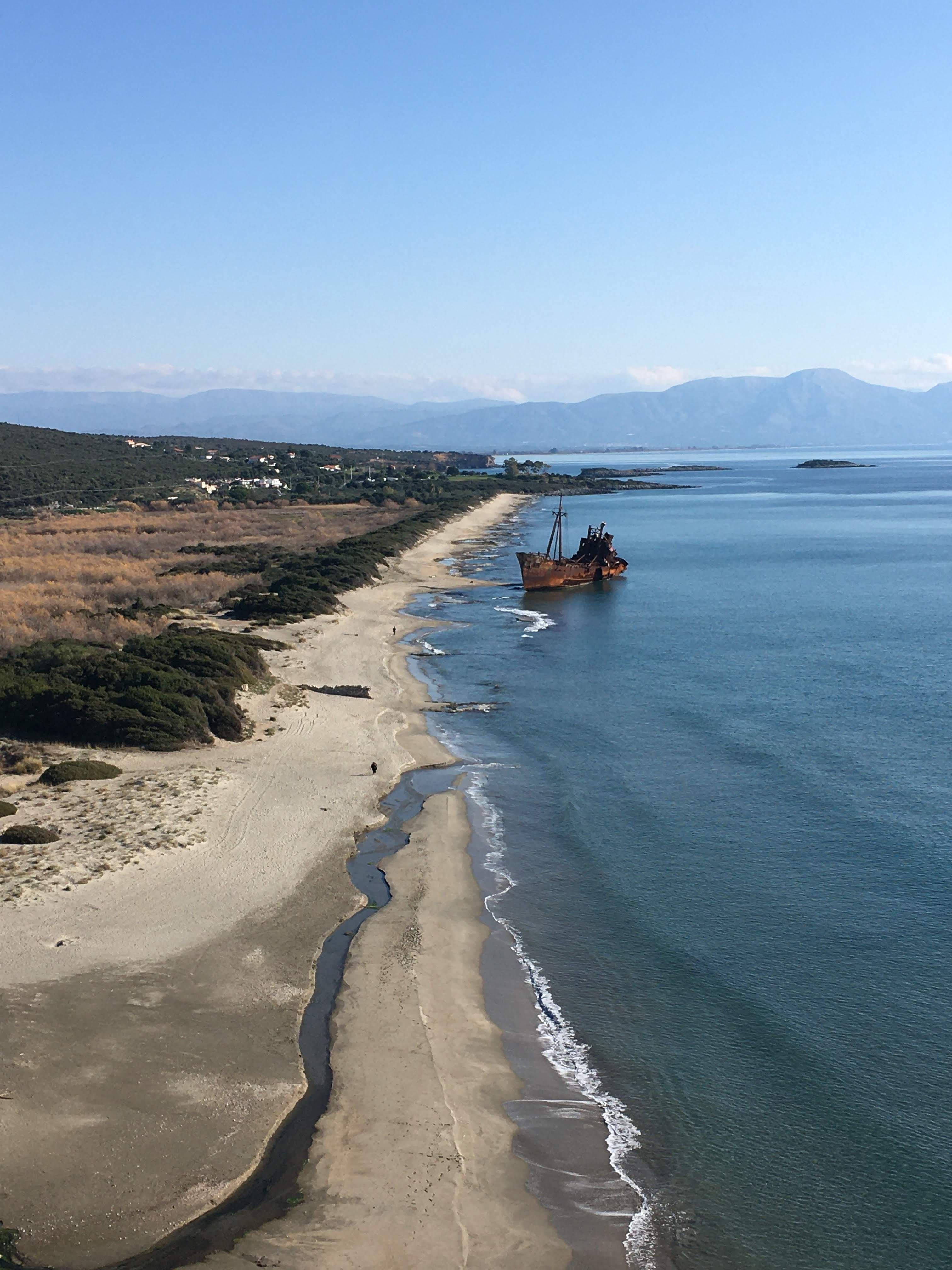 Aerial view of a sandy beach with a shipwreck along the blue ocean, capturing serene coastal beauty.