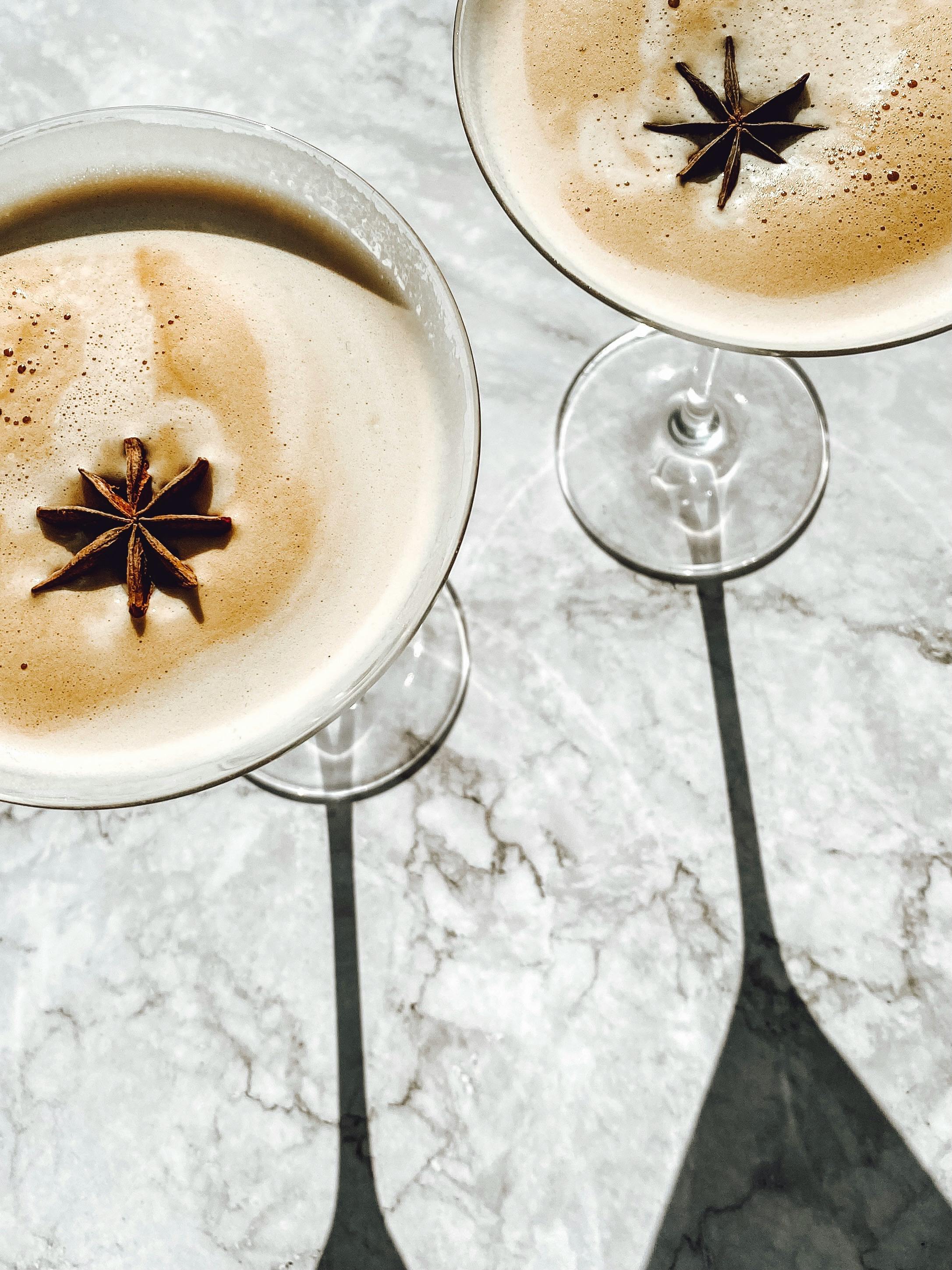 Top view of espresso martinis garnished with star anise, casting shadows on a marble surface.