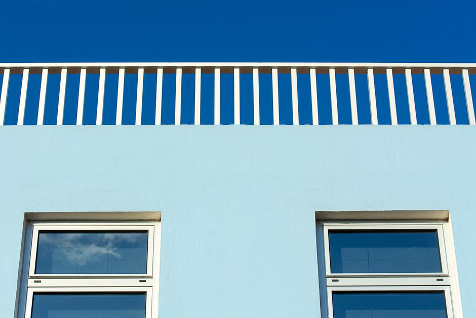 Low angle view of a modern building facade with windows and balustrade against a clear blue sky.